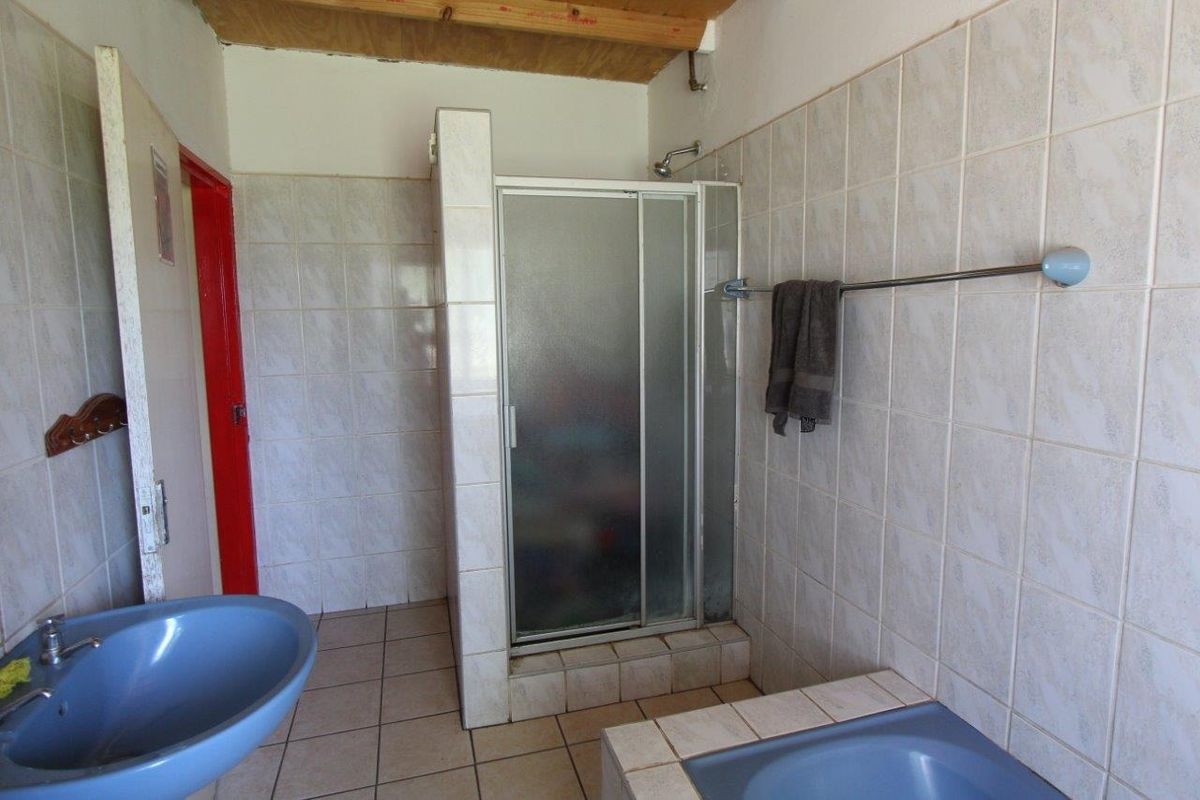 A dated bathroom featuring a shower enclosure, tiled walls, and blue sanitary fixtures, with exposed wooden ceiling beams.