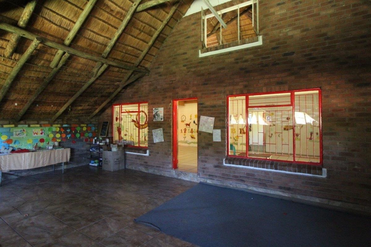 Spacious interior room featuring exposed thatch roof, brick walls, and tiled flooring, currently utilized as a play area with large windows.