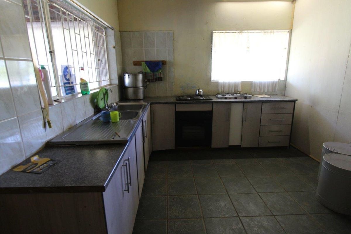 A functional kitchen featuring L-shaped cabinetry, a stainless steel sink, built-in oven, and gas hob, with tiled flooring and security bars on the windows.