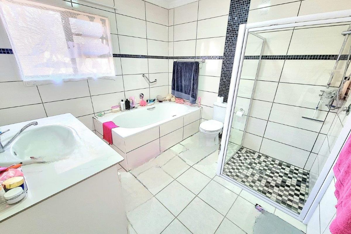 A functional bathroom featuring a built-in bathtub, a separate glass-enclosed shower, a vanity basin, and a toilet with tiled walls and flooring.