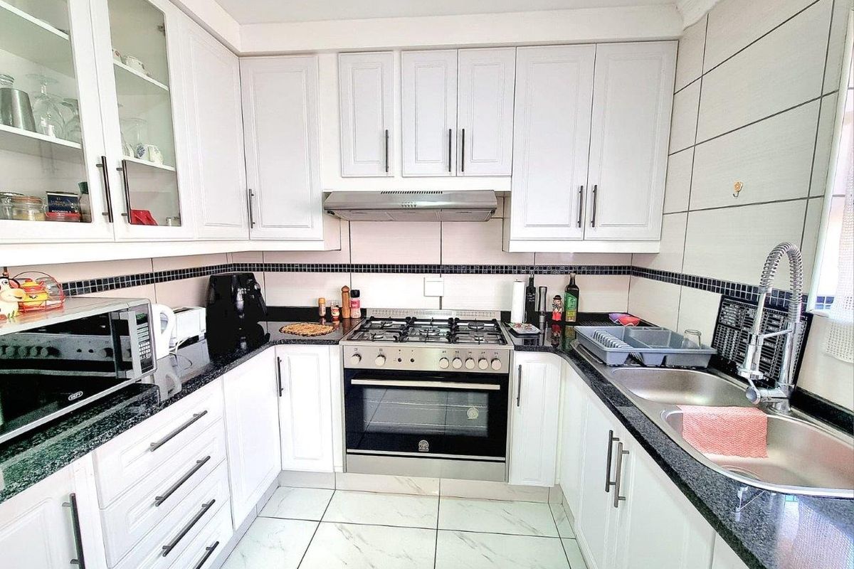 A well-maintained kitchen featuring white cabinetry, granite countertops, a built-in oven with gas hob, extractor fan, and a double stainless steel sink.