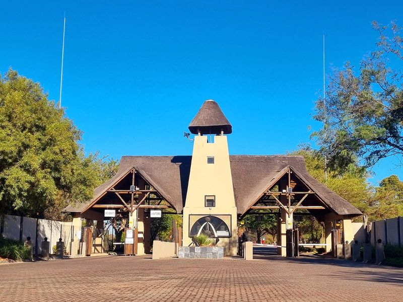 A well-maintained residential estate entrance gatehouse featuring a thatched roof, paved driveway, and dedicated access lanes for residents and visitors.