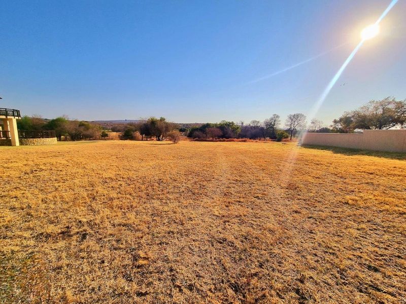 A wide-angle view of a vacant residential plot featuring dry grass, perimeter walling, and distant natural landscape views.