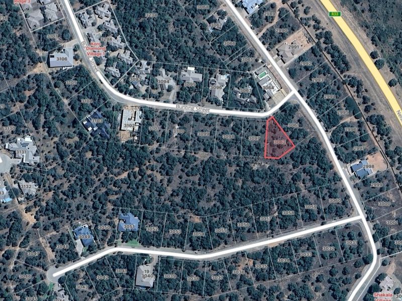 Aerial view of a vacant residential plot highlighted in red, situated within a developed estate with established vegetation.