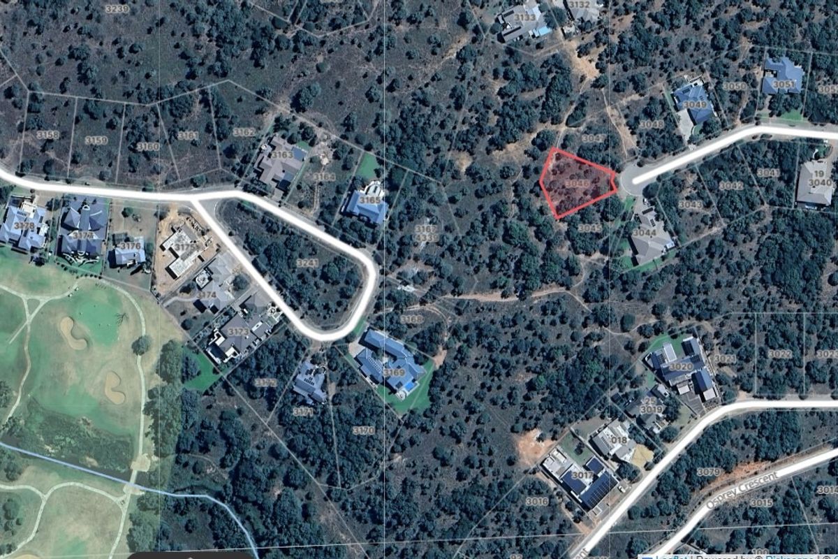 An aerial view of a vacant residential plot highlighted in red, situated within a wooded estate environment.