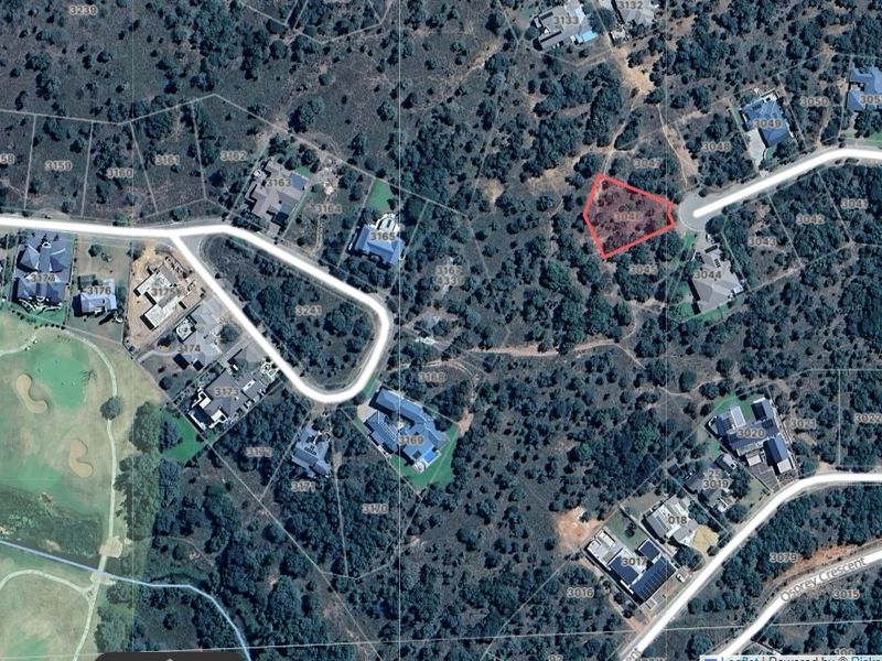 An aerial view of a vacant residential plot highlighted in red, situated within a wooded estate environment.