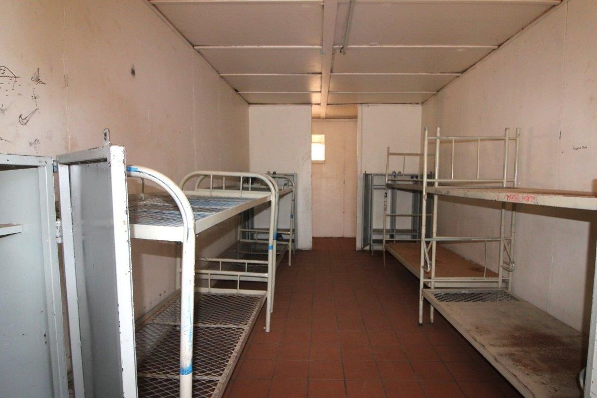 A utilitarian dormitory-style room featuring tiled flooring and basic wall finishes, currently configured with multiple metal bunk bed frames.