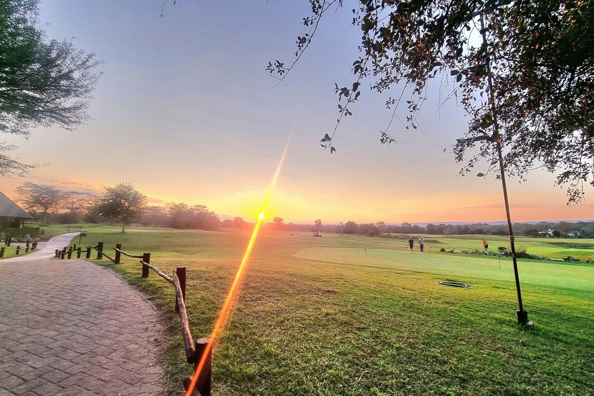 A scenic sunset view overlooking a well-maintained golf course with a paved walkway and rustic timber fencing in the foreground.