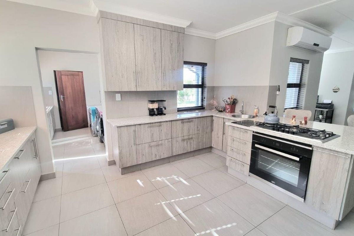 Modern kitchen featuring light wood-grain cabinetry, stone countertops, a built-in oven with gas hob, and an adjacent scullery area.