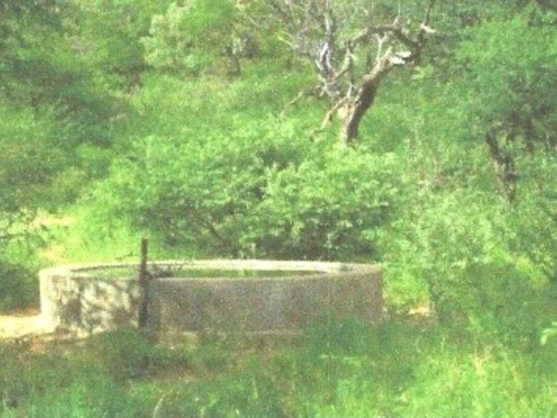 A circular concrete water reservoir located in a natural farm setting, featuring basic infrastructure for water storage.