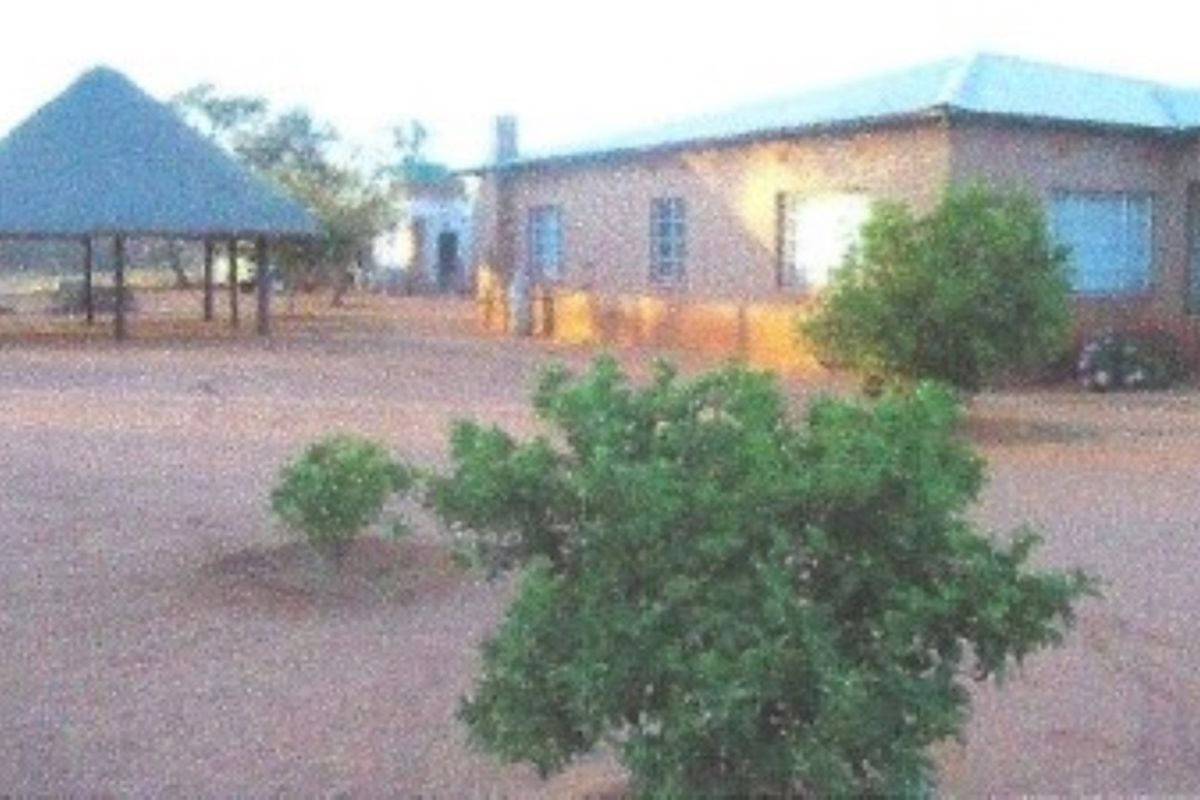 Rear view of the farm property featuring a main dwelling with a metal roof and a separate thatched lapa structure in the yard.