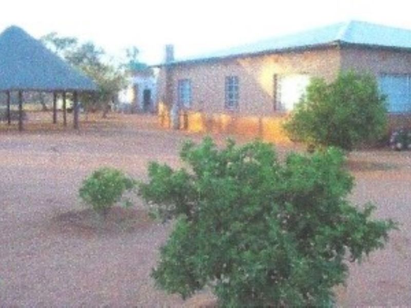 Rear view of the farm property featuring a main dwelling with a metal roof and a separate thatched lapa structure in the yard.