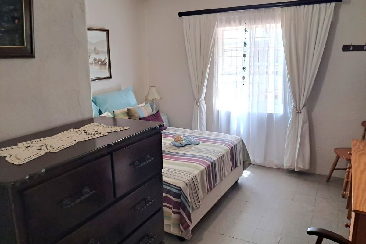 A functional bedroom featuring tiled flooring, a window with curtain rods, and neutral wall finishes.