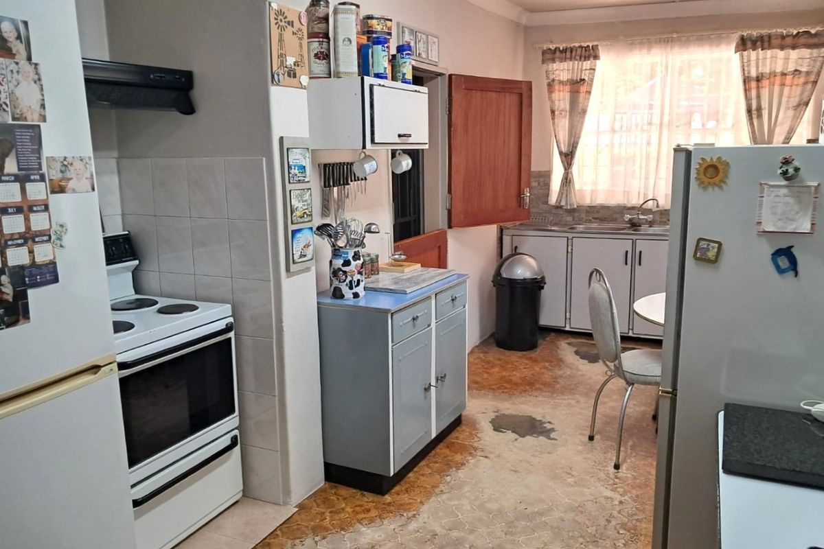 A functional kitchen area featuring built-in cabinetry, a freestanding stove with extractor fan, and a double sink setup with tiled splashbacks.