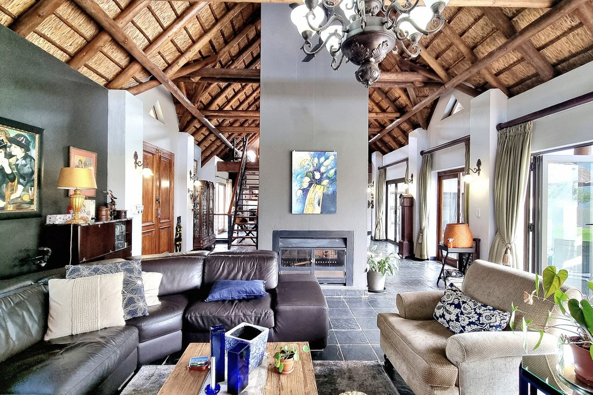 Spacious living room featuring a high vaulted thatched ceiling with exposed timber beams, a central fireplace, and large glass doors leading to the outdoors.