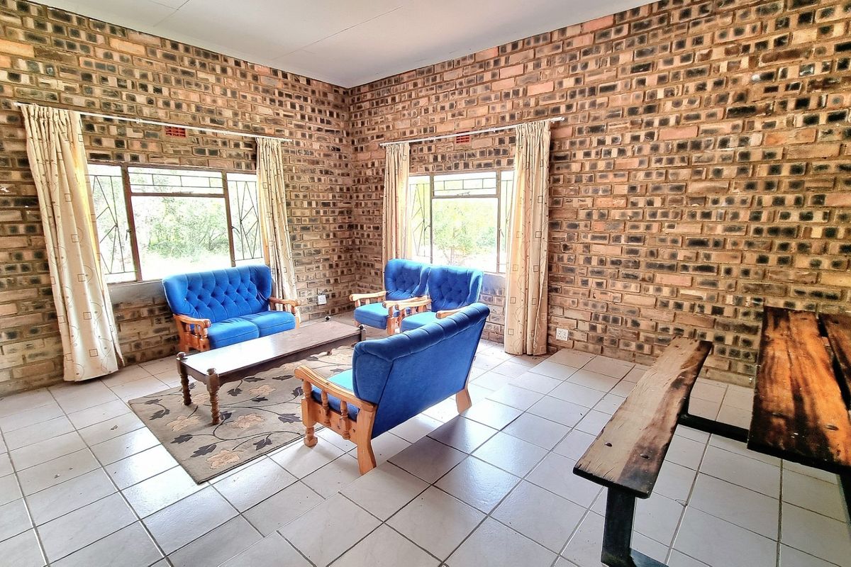 A rustic living area featuring exposed face-brick walls, tiled flooring, and large windows that provide natural light and views of the surrounding farm landscape.