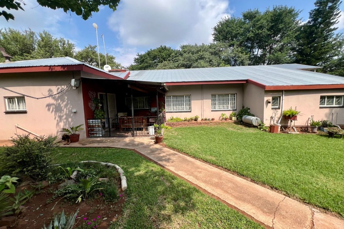 Rear view of the farmhouse featuring a covered patio area, corrugated metal roof, and a well-maintained lawn with a concrete pathway.