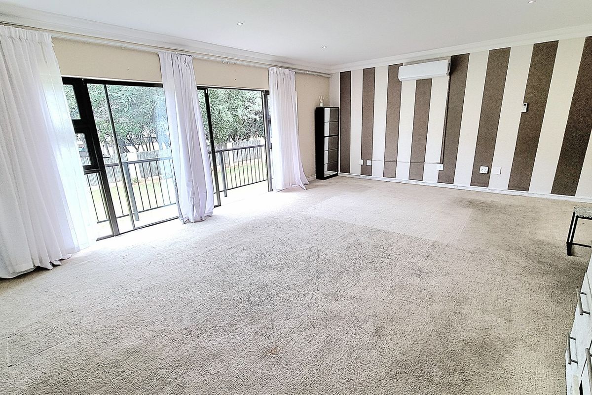 Spacious living area featuring large sliding glass doors leading to a balcony, wall-mounted air conditioning unit, and neutral striped feature wall.