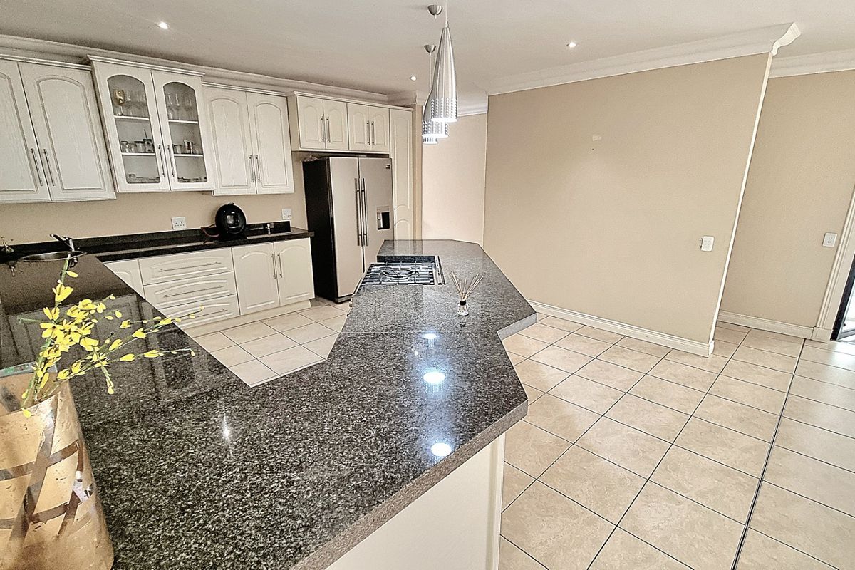 Spacious kitchen featuring granite countertops, white cabinetry, a central island with a built-in gas hob, and tiled flooring with direct outdoor access.