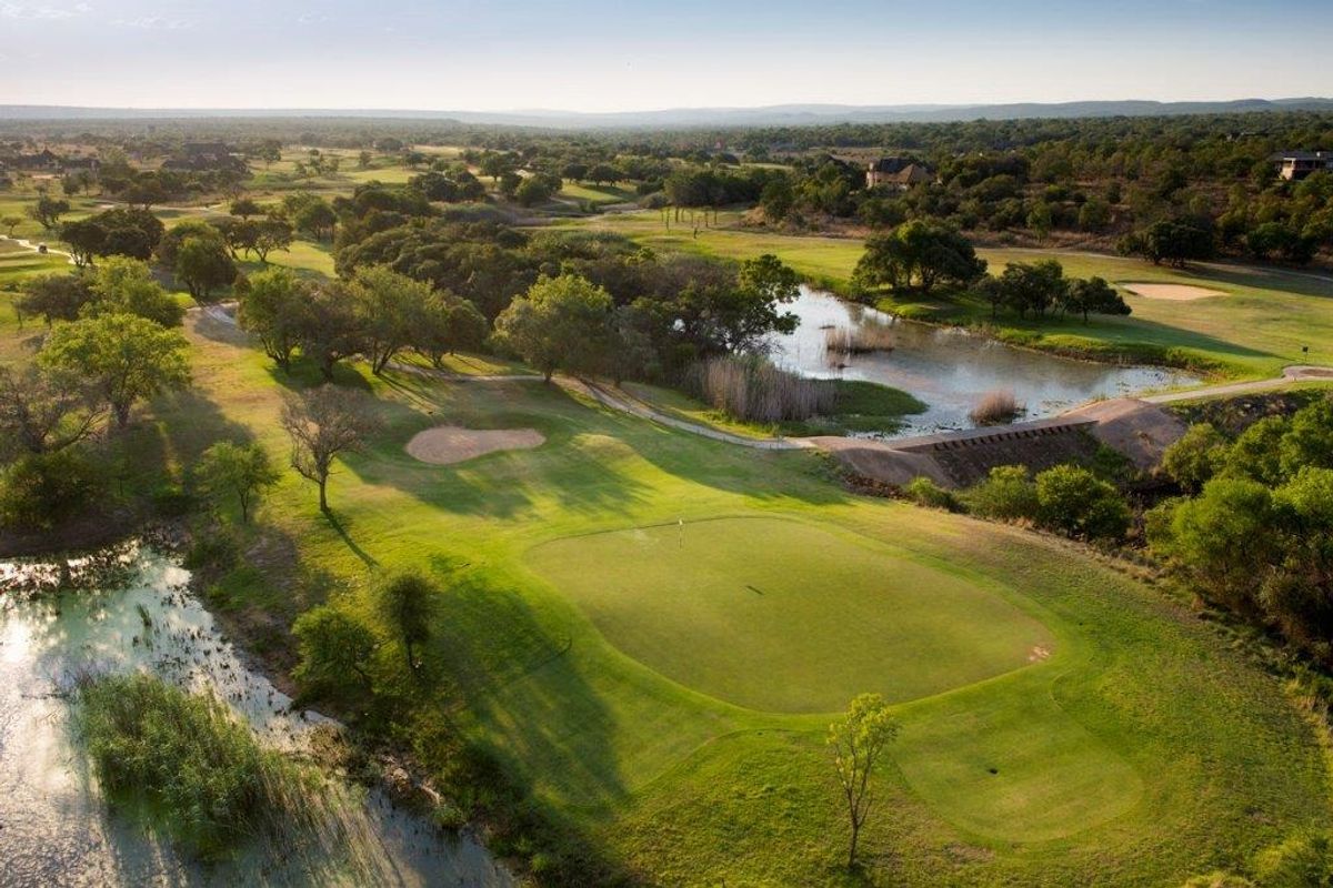An elevated aerial view of a lush green golf course landscape featuring water hazards and natural vegetation.