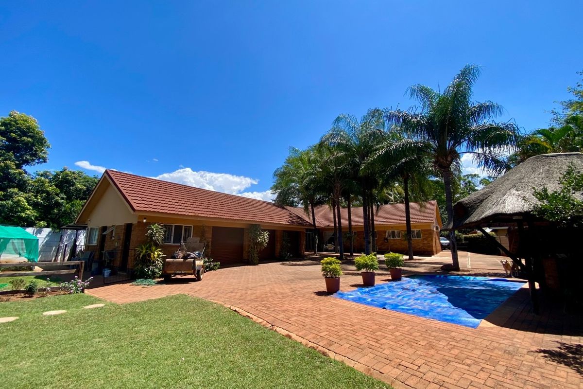 Spacious rear exterior featuring a brick-paved courtyard, swimming pool with cover, and a traditional thatched lapa, set against a well-maintained garden.