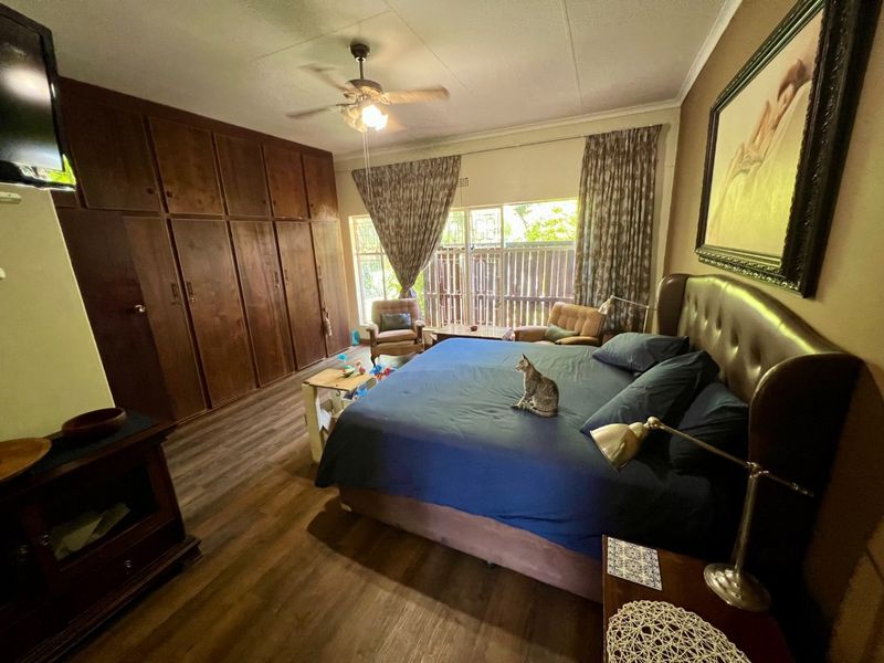 Spacious bedroom featuring extensive built-in wooden cabinetry, laminate flooring, and a ceiling fan, with large windows providing natural light.