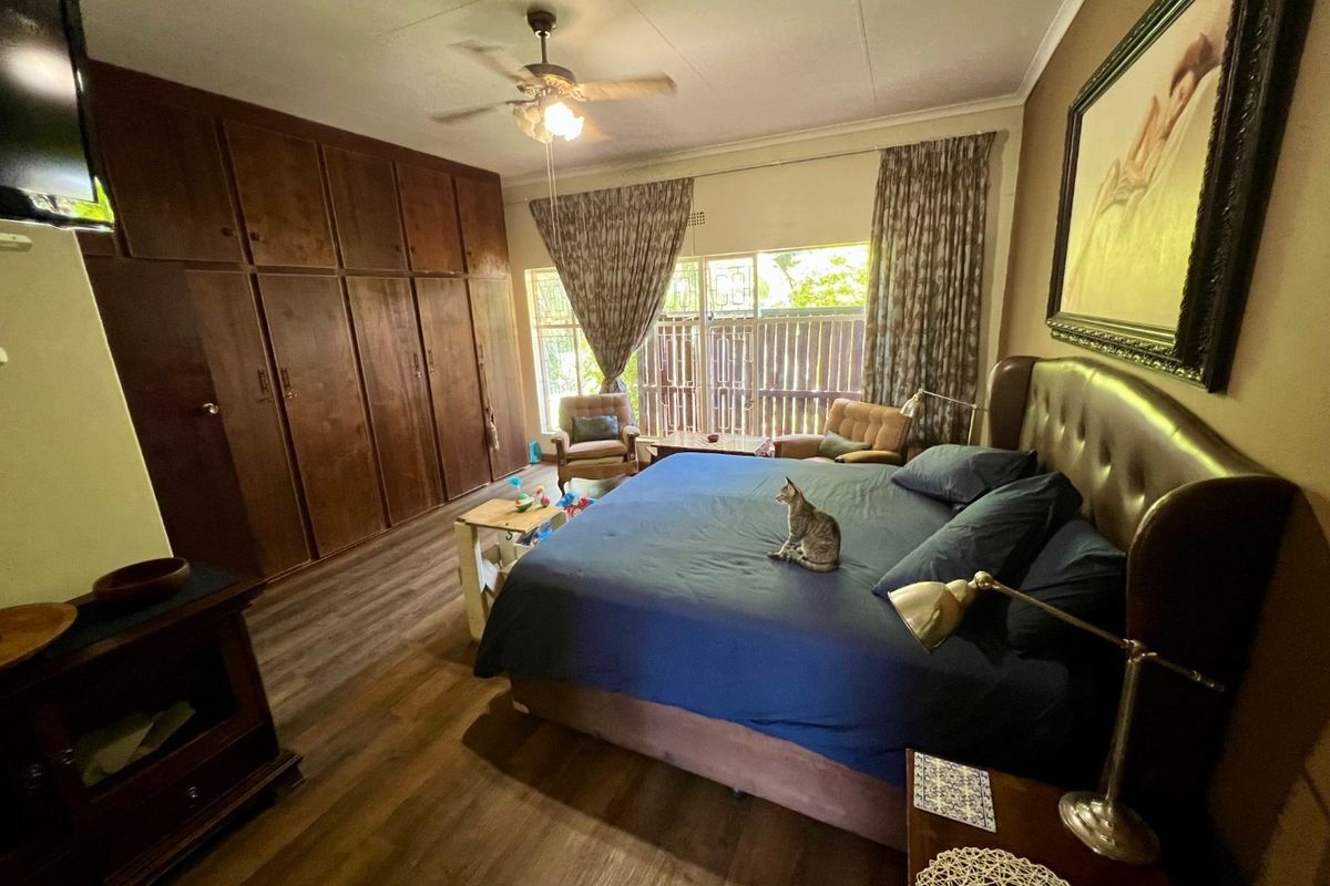Spacious bedroom featuring extensive built-in wooden cabinetry, laminate flooring, and a ceiling fan, with large windows providing natural light.