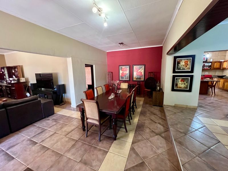 Spacious open-plan dining and living area featuring ceramic tile flooring and a bold red accent wall, connecting seamlessly to the kitchen space.