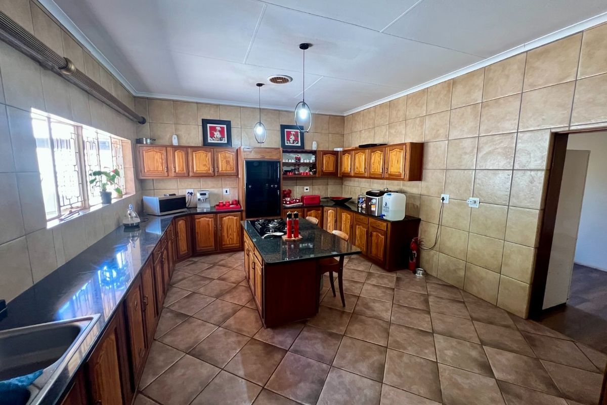 Spacious kitchen featuring wooden cabinetry, granite countertops, a central island with a built-in gas hob, and full-height wall tiling.