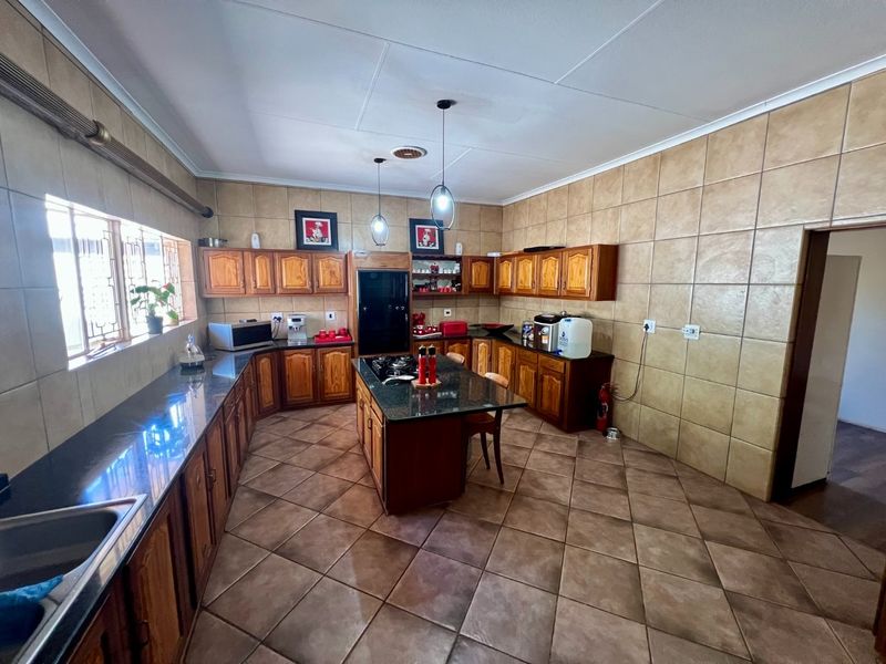 Spacious kitchen featuring wooden cabinetry, granite countertops, a central island with a built-in gas hob, and full-height wall tiling.