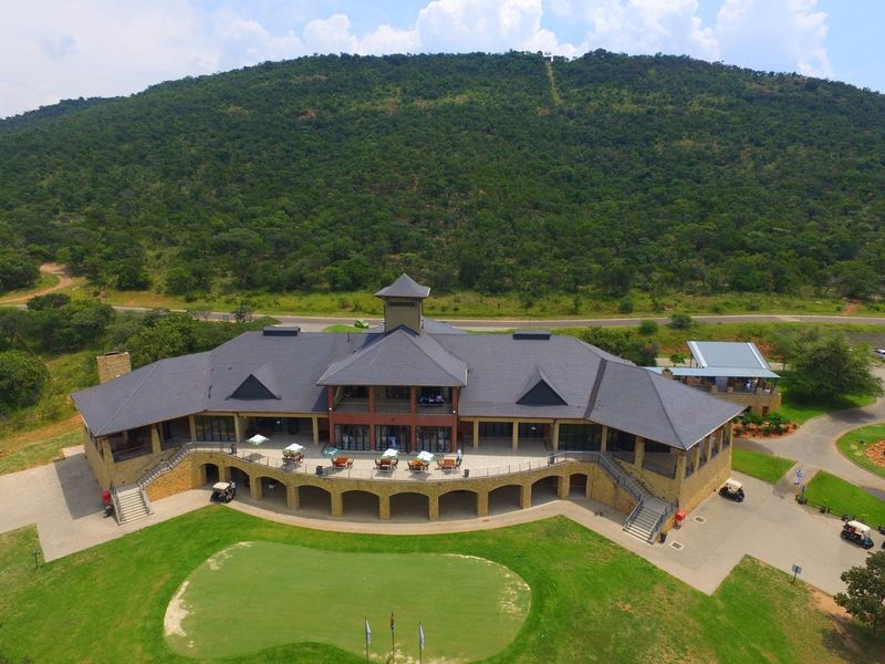 Aerial view of a large clubhouse facility featuring stone masonry, expansive covered patios, and direct access to a golf course in a scenic setting.