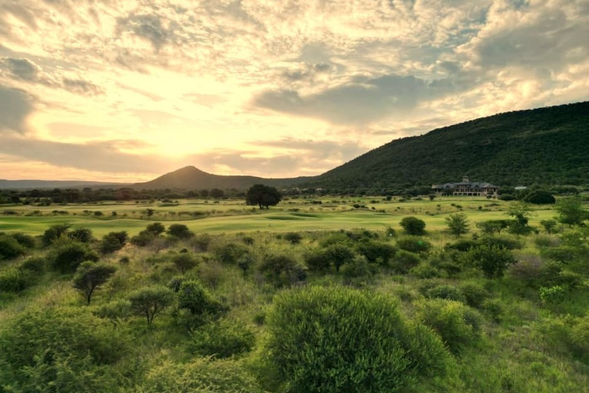 A scenic landscape view of a golf course set against rolling hills and a sunset sky.