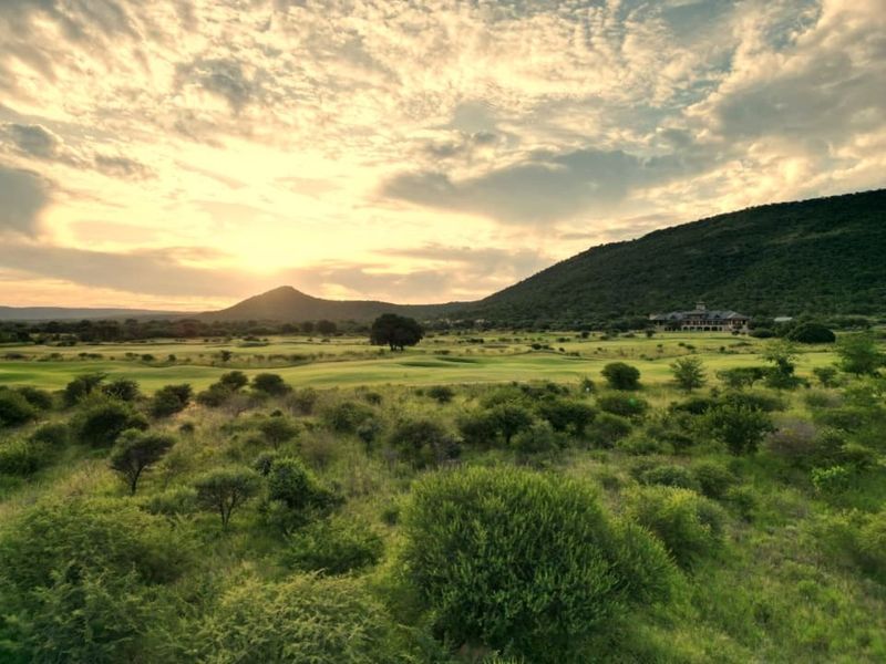 A scenic landscape view of a golf course set against rolling hills and a sunset sky.