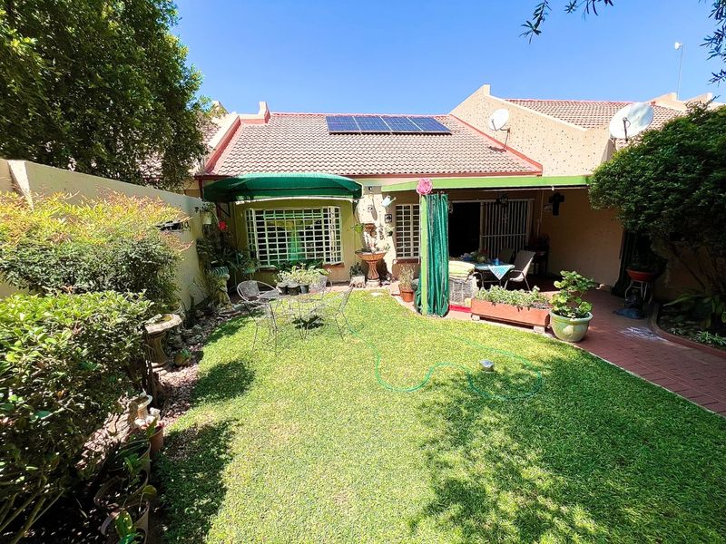 Rear view of the townhouse featuring a private garden, paved patio area, and roof-mounted solar panels.