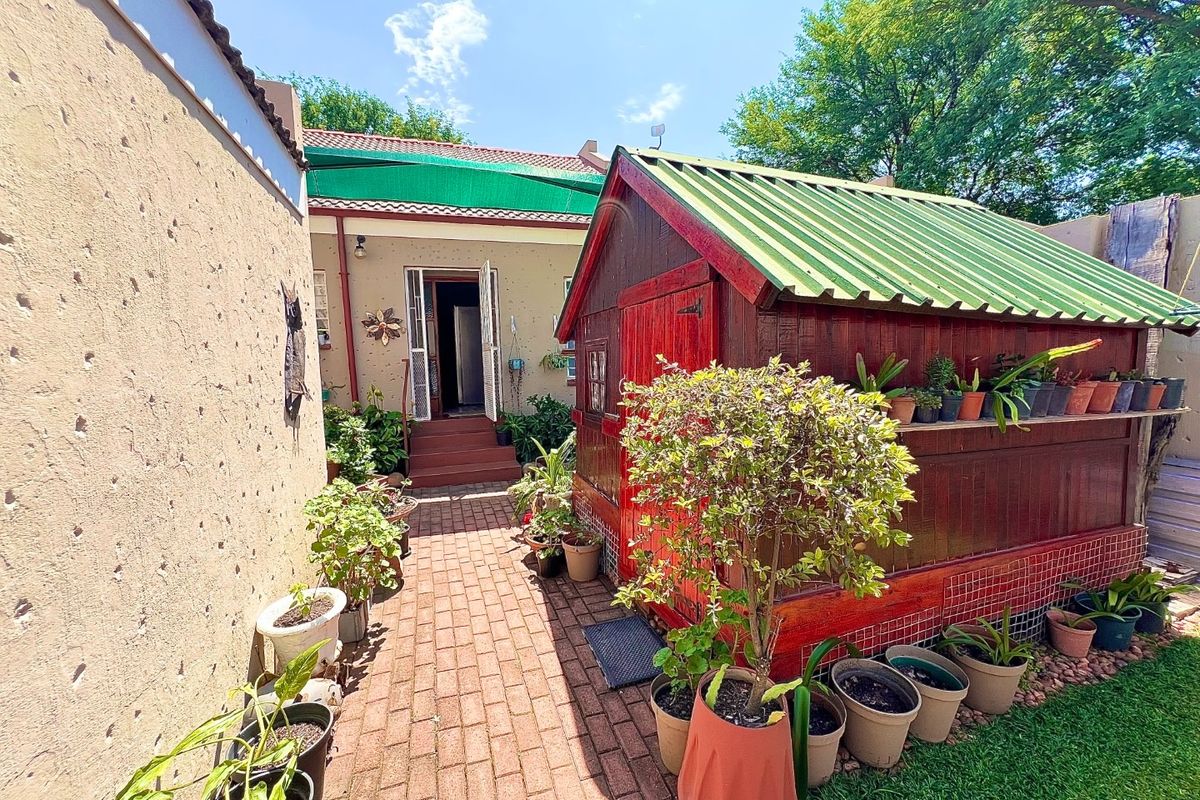 Rear courtyard area featuring brick paving, a timber garden shed with a corrugated roof, and access to the main dwelling via a security gate.
