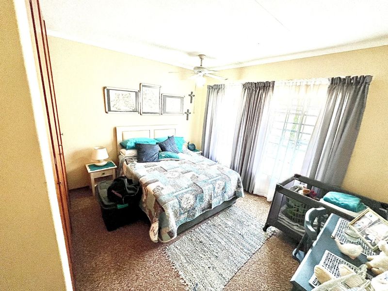 A bedroom featuring a ceiling fan, built-in cupboard, and large windows with curtain rails, providing natural light and functional storage space.