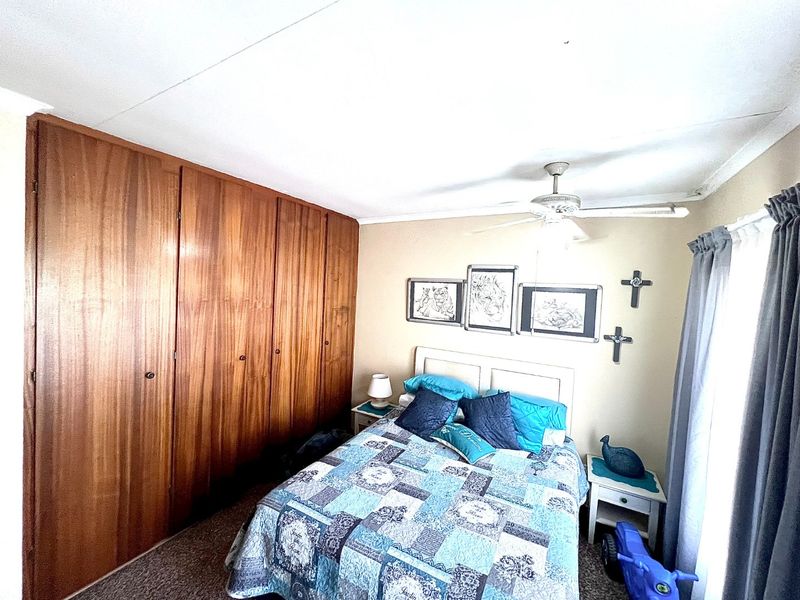 A bedroom featuring built-in wooden cupboards and a ceiling fan, offering functional storage and climate control.