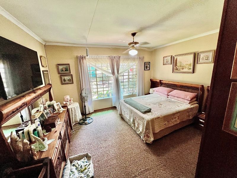 A carpeted bedroom featuring a ceiling fan and security bars on the windows, offering a functional and lived-in space.