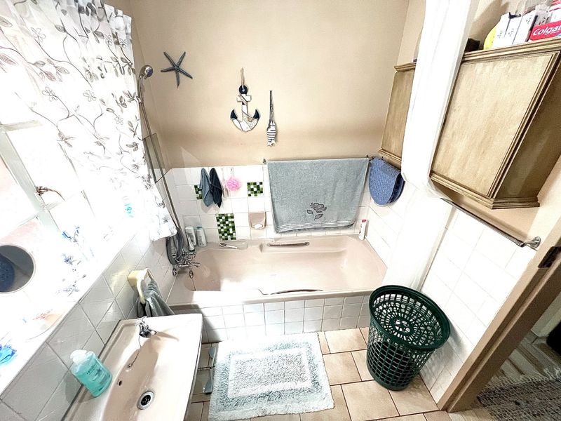 A functional bathroom featuring a built-in bathtub with shower attachment, pedestal sink, and built-in cabinetry, finished with tiled splashbacks.