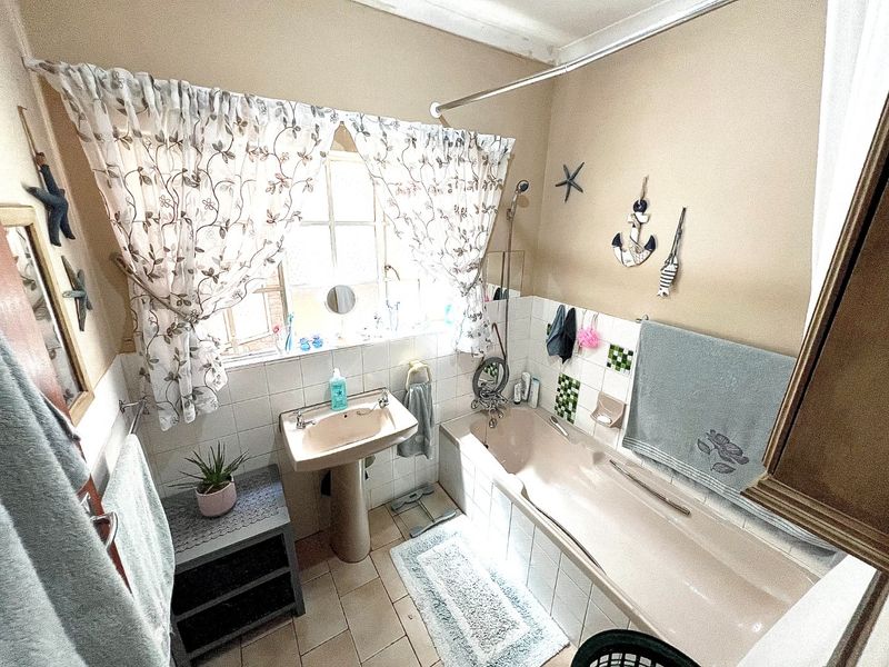 A dated bathroom featuring a pedestal sink, bathtub with shower attachment, and tiled finishes, offering potential for a modern renovation.