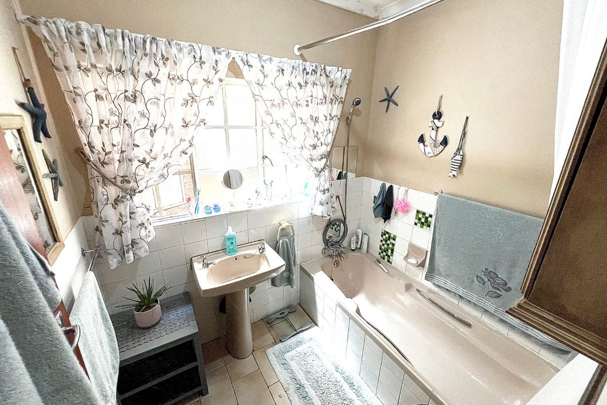 A dated bathroom featuring a pedestal sink, bathtub with shower attachment, and tiled finishes, offering potential for a modern renovation.