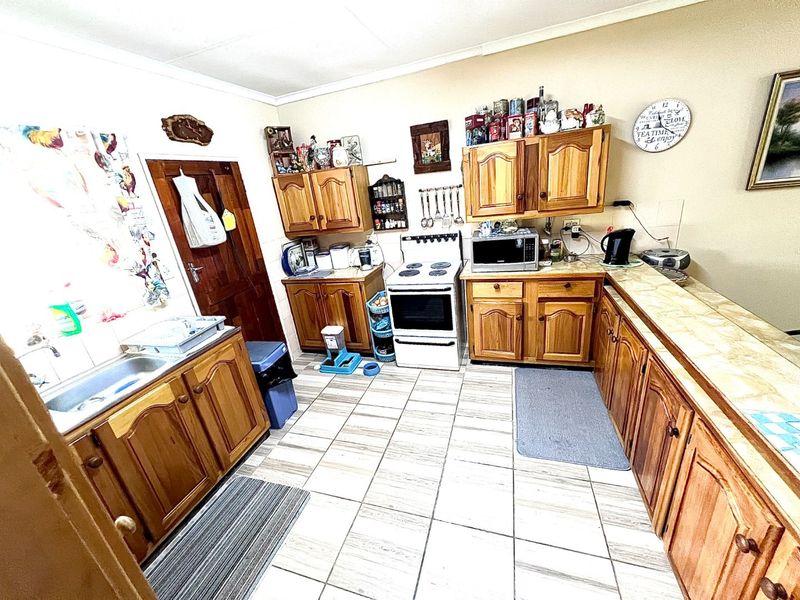 A functional kitchen featuring wooden cabinetry, tiled countertops, and tiled flooring, offering a traditional layout with ample storage space.