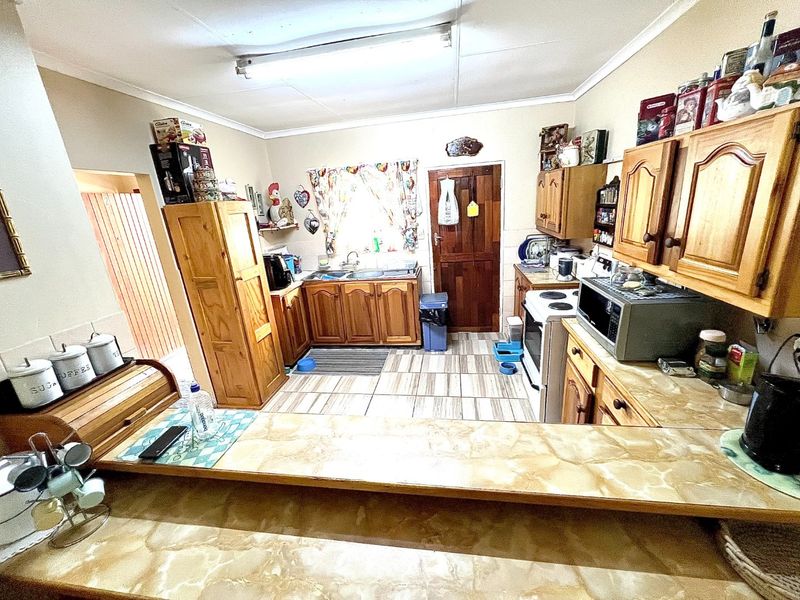 A functional kitchen featuring wooden cabinetry, laminate countertops, and tiled flooring, offering a traditional layout with potential for modern updates.