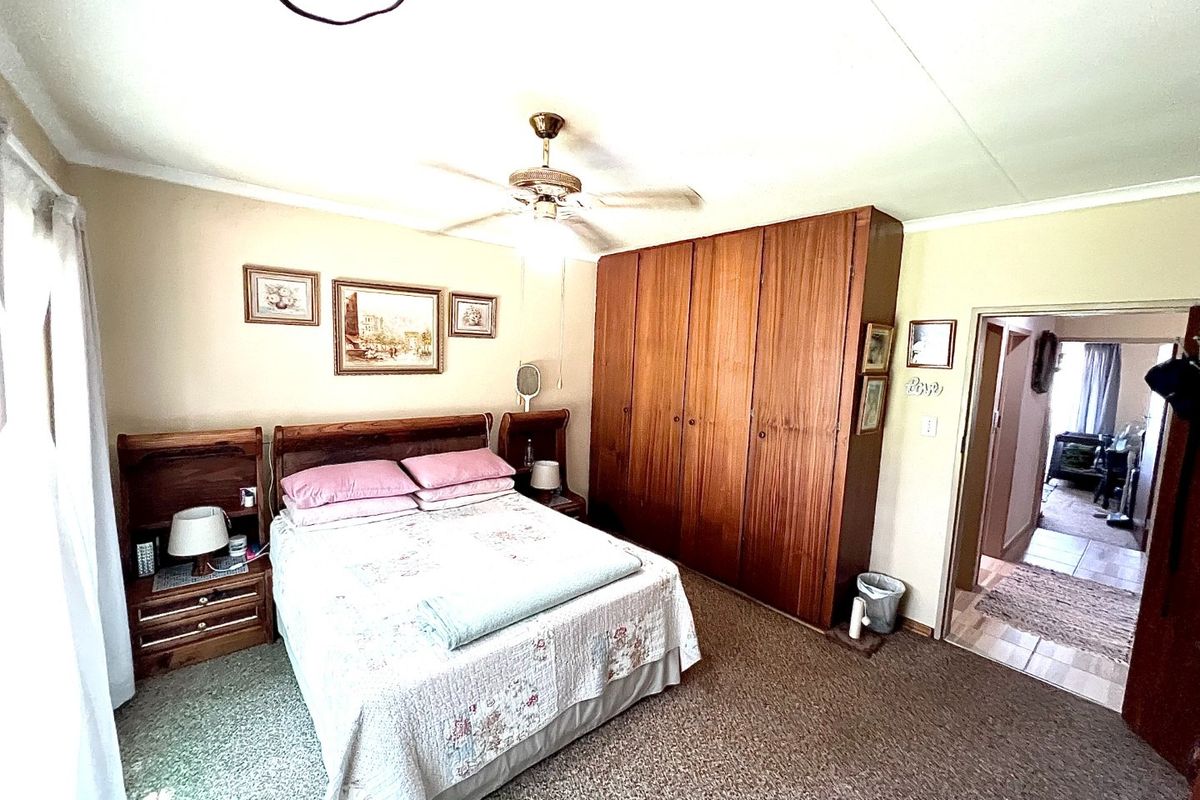 A bedroom featuring built-in wooden cupboards, a ceiling fan, and carpeted flooring, with an adjacent hallway visible.