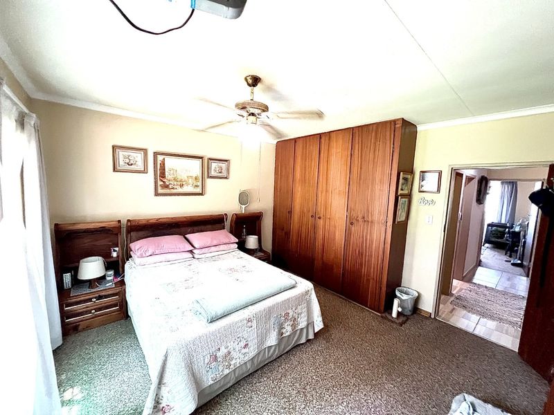 A bedroom featuring built-in wooden cupboards, a ceiling fan, and carpeted flooring, with an adjacent hallway visible.