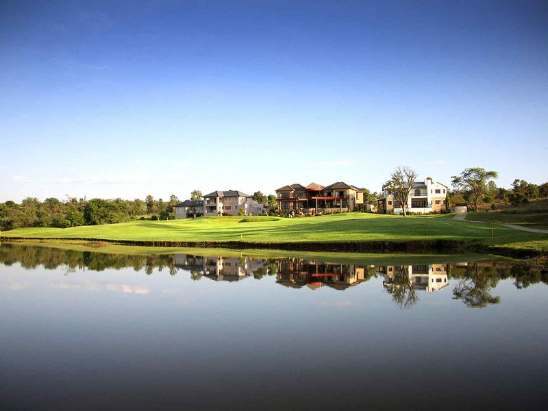 A scenic view of a golf course and lake with residential properties in the background.