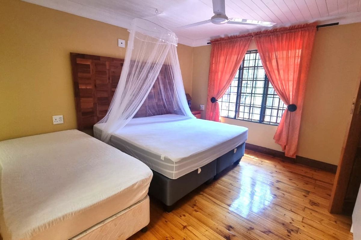 A bedroom featuring polished timber flooring, a ceiling fan, and a window fitted with security bars.