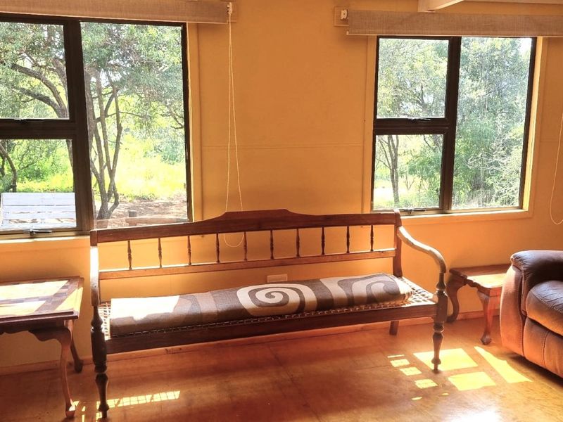 A sunlit living area featuring timber flooring and large windows with roller blinds, offering a pleasant view of the surrounding trees.