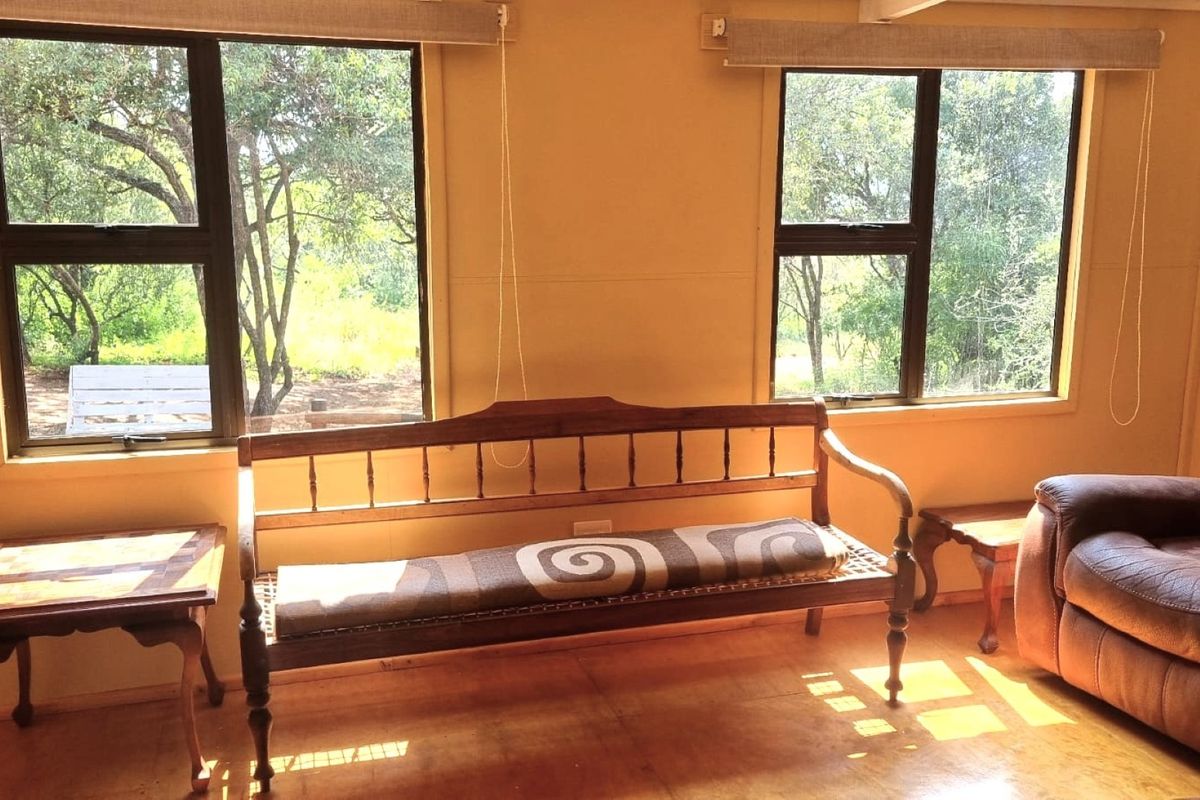 A sunlit living area featuring timber flooring and large windows with roller blinds, offering a pleasant view of the surrounding trees.