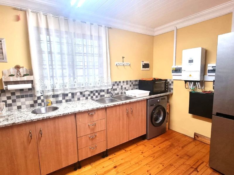 Functional laundry room featuring granite countertops, double stainless steel sink, wooden cabinetry, and integrated inverter system with timber flooring.